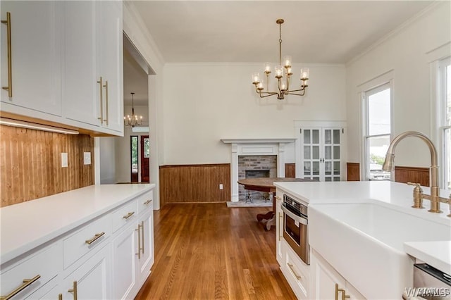 kitchen with sink, a brick fireplace, decorative light fixtures, white cabinetry, and a chandelier