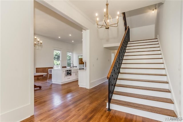 stairway featuring wood-type flooring, a notable chandelier, and ornamental molding