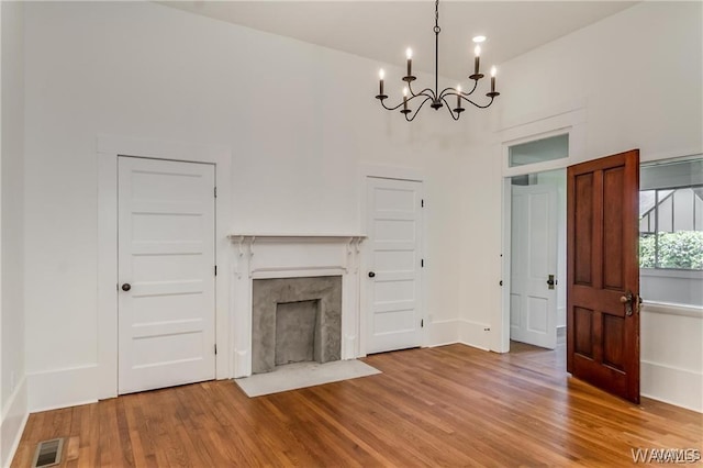 unfurnished living room with hardwood / wood-style flooring, a fireplace, a high ceiling, and a chandelier