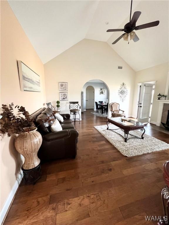 living room with ceiling fan, dark hardwood / wood-style floors, high vaulted ceiling, and a tile fireplace