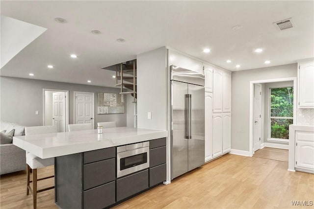 kitchen featuring light stone countertops, built in appliances, light hardwood / wood-style flooring, white cabinetry, and a breakfast bar area