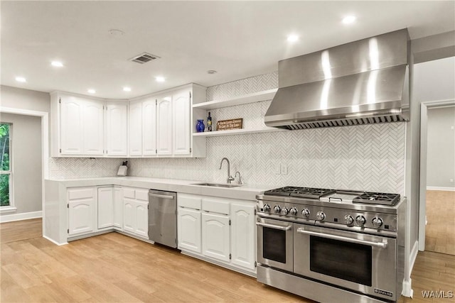 kitchen featuring white cabinets, appliances with stainless steel finishes, wall chimney exhaust hood, and sink