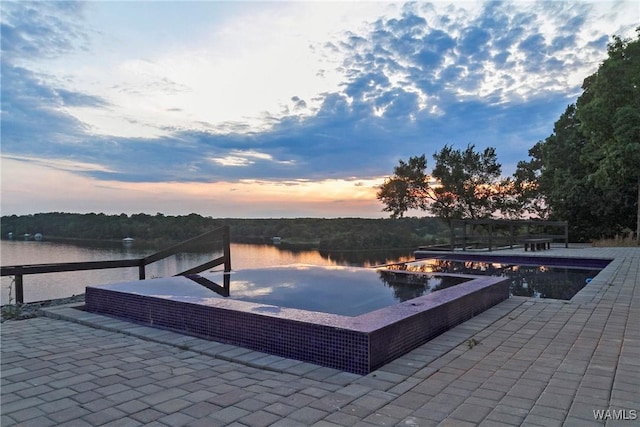 pool at dusk featuring a patio area and a water view