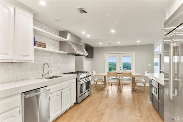 kitchen with white cabinetry, sink, wall chimney range hood, built in appliances, and light wood-type flooring