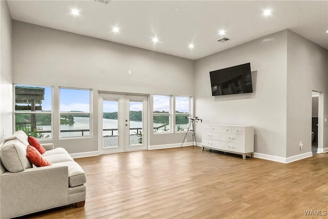 living room with french doors, a towering ceiling, and hardwood / wood-style flooring