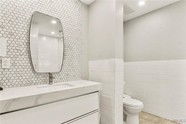 bathroom with tile patterned flooring, vanity, toilet, and tile walls