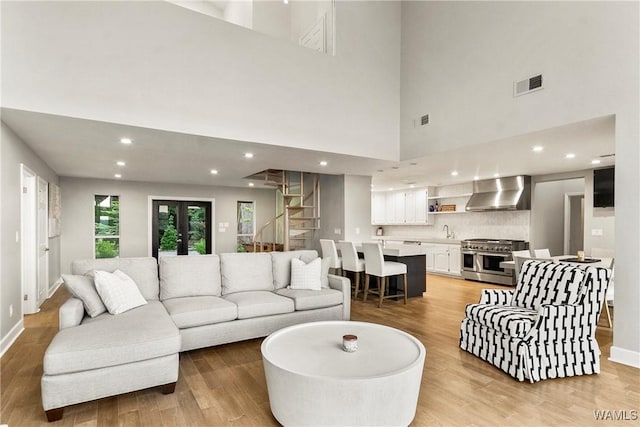 living room with a towering ceiling, light wood-type flooring, and sink