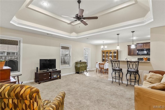 living room with a tray ceiling, light colored carpet, baseboards, and ceiling fan with notable chandelier