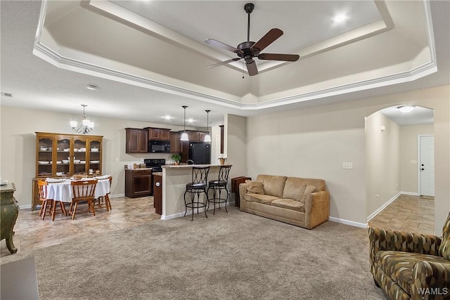 living room with arched walkways, a raised ceiling, and light colored carpet