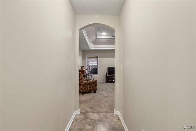 hallway featuring arched walkways, a textured ceiling, light carpet, and baseboards