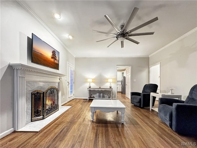 living room with a premium fireplace, ornamental molding, hardwood / wood-style floors, and ceiling fan