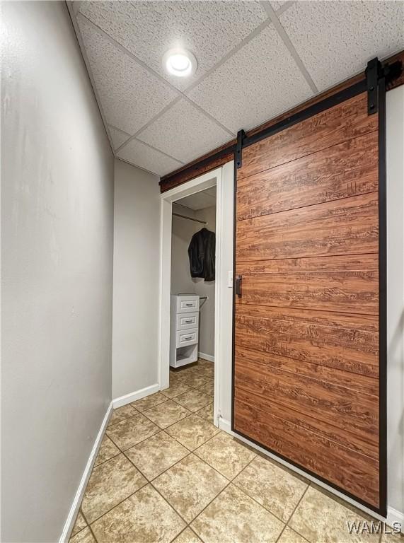 corridor featuring a drop ceiling, light tile patterned floors, and a barn door