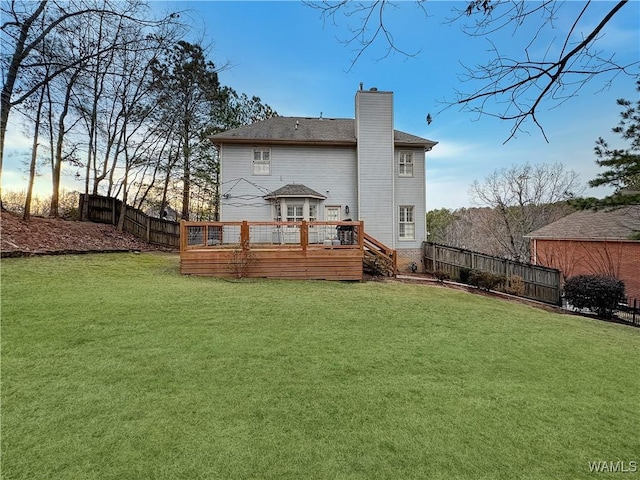 back house at dusk with a wooden deck and a yard