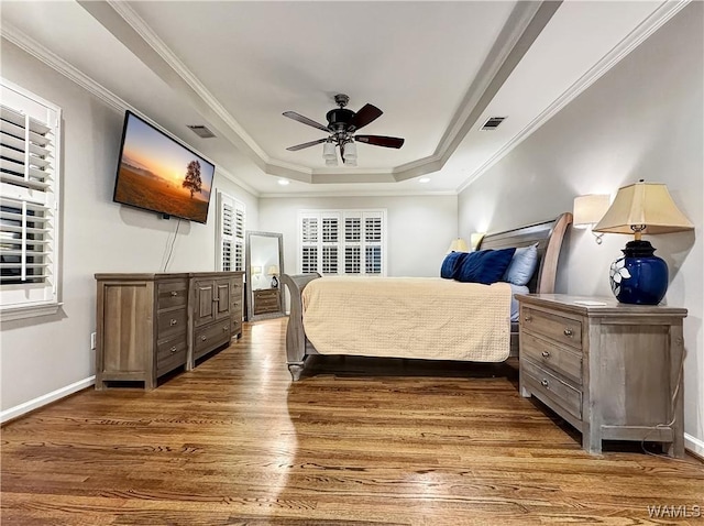 bedroom with ornamental molding, wood-type flooring, and a tray ceiling