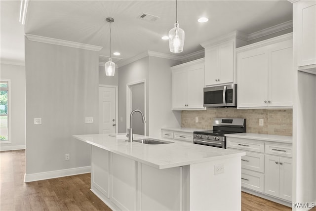 kitchen with white cabinetry, sink, stainless steel appliances, pendant lighting, and a center island with sink