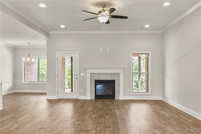 unfurnished living room featuring a tiled fireplace, ornamental molding, ceiling fan with notable chandelier, and hardwood / wood-style flooring