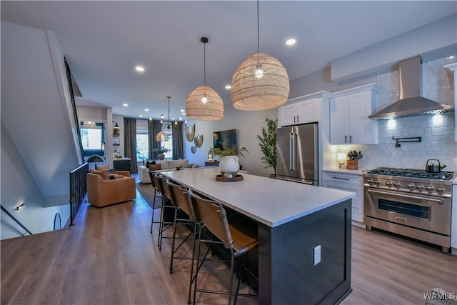 kitchen with white cabinets, wall chimney exhaust hood, high quality appliances, open floor plan, and light countertops