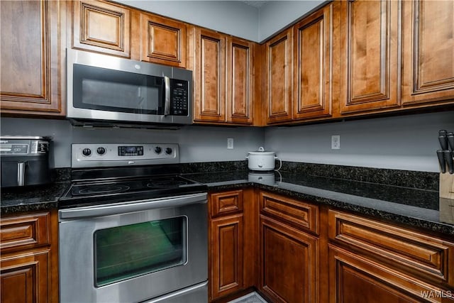 kitchen featuring brown cabinets, stainless steel appliances, and dark stone counters