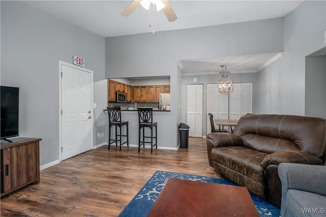 living area with dark wood finished floors, ceiling fan with notable chandelier, high vaulted ceiling, and baseboards