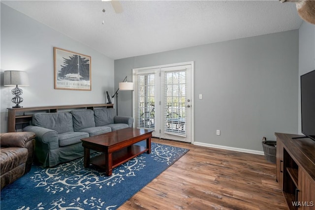 living area featuring vaulted ceiling, a textured ceiling, baseboards, and wood finished floors