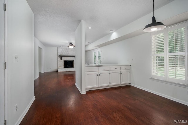 4410 Nicholas Ave, Northport, AL 35473 - unfurnished living room with a ceiling fan, dark wood-style flooring, a brick fireplace, a textured ceiling, and recessed lighting