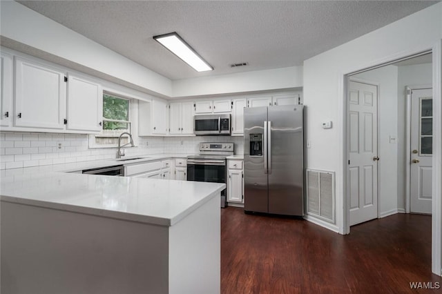4410 Nicholas Ave, Northport, AL 35473 - kitchen with appliances with stainless steel finishes, dark wood-style flooring, backsplash, a peninsula, and white cabinetry