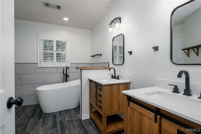4410 Nicholas Ave, Northport, AL 35473 - bathroom featuring tile walls, two vanities, a freestanding bath, wainscoting, and wood finished floors