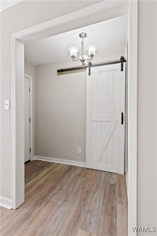 unfurnished dining area featuring a barn door, a notable chandelier, and hardwood / wood-style flooring