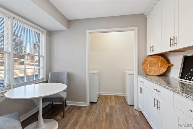 kitchen featuring washing machine and dryer, white cabinetry, light hardwood / wood-style floors, and light stone counters