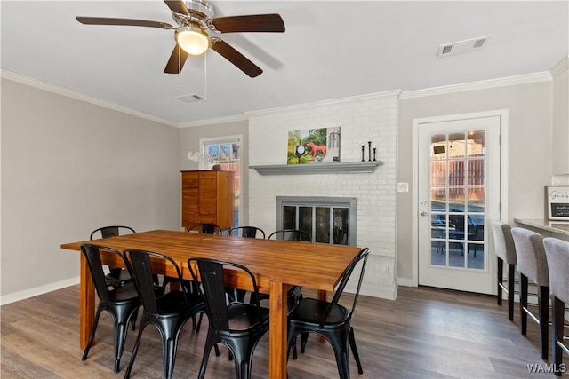 dining room with ceiling fan, a fireplace, crown molding, and dark wood-type flooring