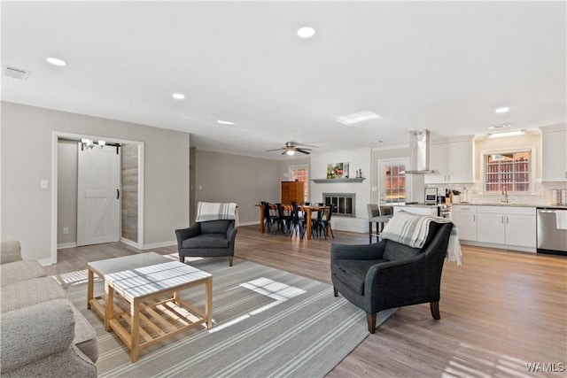 living room with ceiling fan, sink, a barn door, and light wood-type flooring