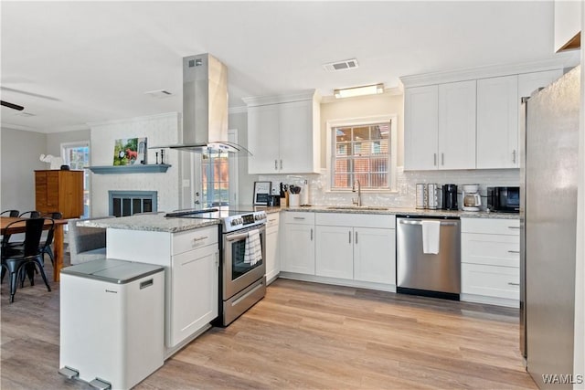 kitchen with kitchen peninsula, sink, island exhaust hood, stainless steel appliances, and white cabinets