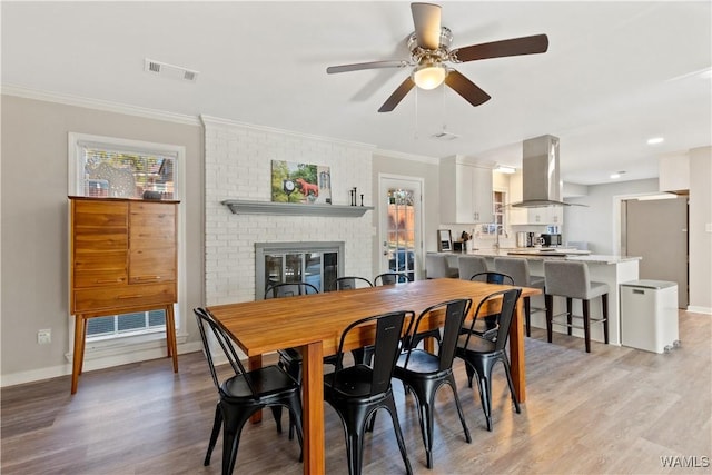 dining room featuring ceiling fan, crown molding, a fireplace, and light hardwood / wood-style flooring