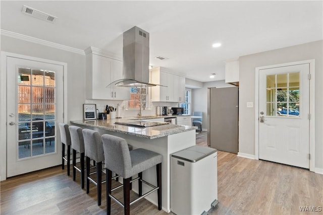 kitchen featuring island range hood, kitchen peninsula, stainless steel fridge, white cabinets, and light stone counters