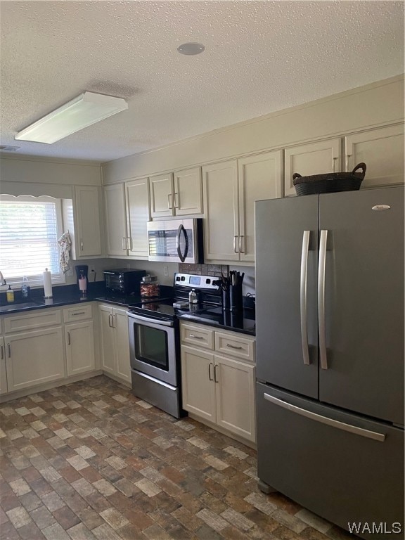 kitchen featuring a textured ceiling, stainless steel appliances, white cabinetry, and a skylight