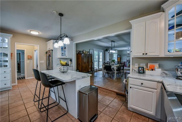 4402 Lakeshore Dr, Northport, AL 35473 - kitchen featuring light tile patterned flooring, white cabinets, a kitchen breakfast bar, decorative light fixtures, and glass insert cabinets