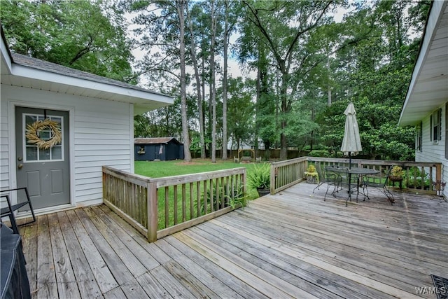 4402 Lakeshore Dr, Northport, AL 35473 - wooden terrace with outdoor dining space, a lawn, an outbuilding, and view of wooded area