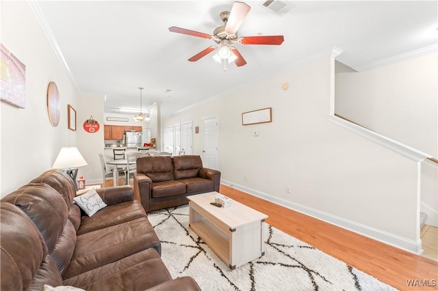 living room with a ceiling fan, baseboards, visible vents, light wood-style floors, and crown molding