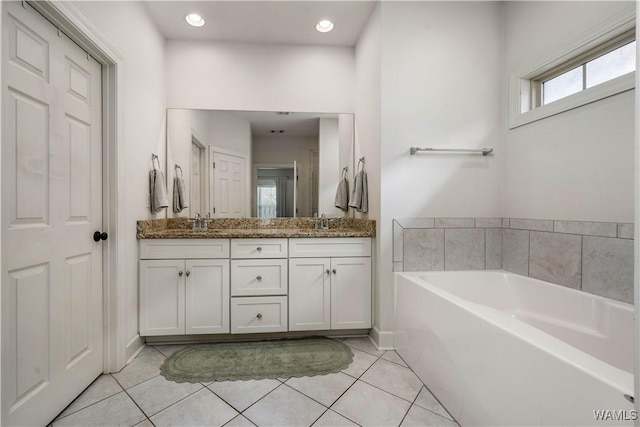 full bathroom featuring tile patterned floors, double vanity, a bath, a sink, and baseboards