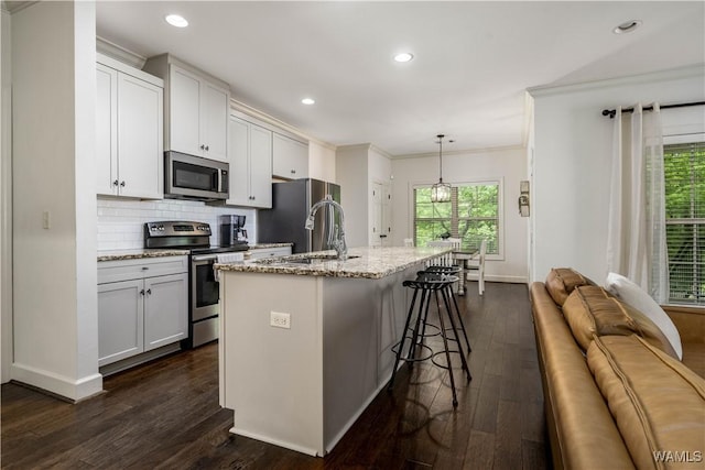 kitchen with a kitchen island with sink, stainless steel appliances, ornamental molding, dark wood-style flooring, and a sink