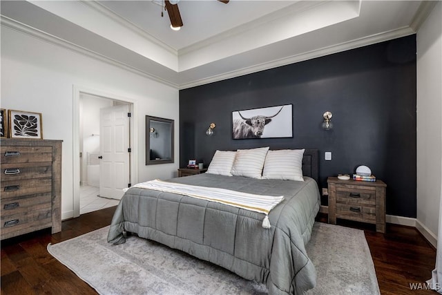 bedroom featuring wood finished floors, ensuite bathroom, baseboards, crown molding, and a tray ceiling