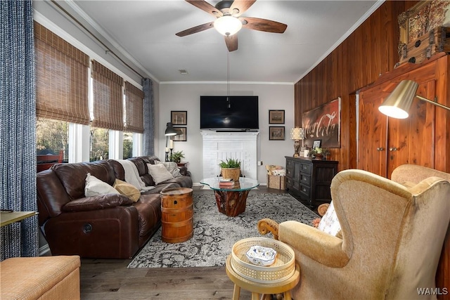 living room with hardwood / wood-style flooring, ceiling fan, wooden walls, ornamental molding, and a brick fireplace