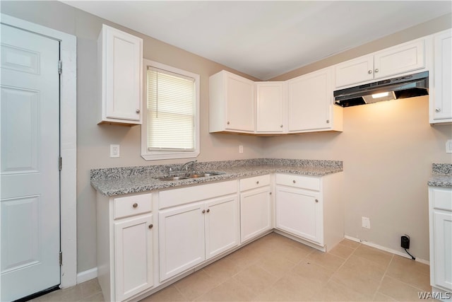 kitchen with light stone countertops, white cabinetry, and sink