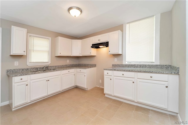 kitchen featuring light stone countertops, white cabinetry, and sink