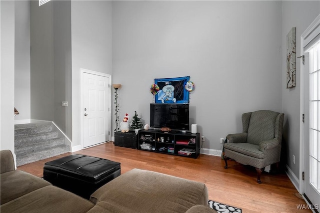 living room featuring stairs, a high ceiling, wood finished floors, and baseboards