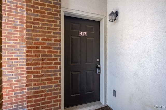 doorway to property featuring brick siding and stucco siding