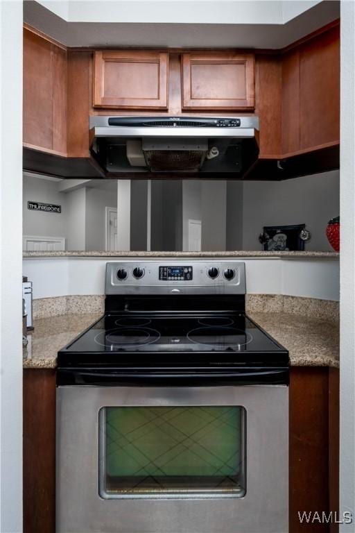 kitchen with stainless steel electric stove, exhaust hood, brown cabinetry, and light countertops