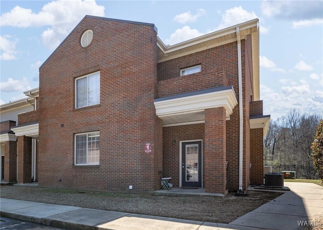 view of front facade featuring brick siding, central AC, and a balcony