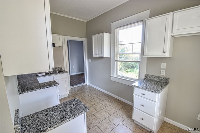 kitchen with white cabinetry, ornamental molding, and dark stone countertops