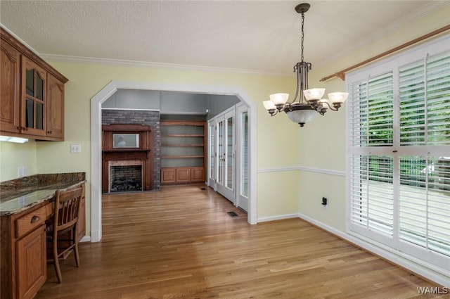 kitchen with an inviting chandelier, crown molding, dark stone counters, pendant lighting, and a fireplace